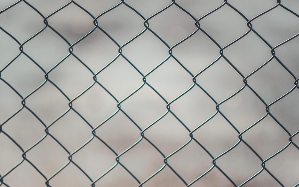 Detailed closeup of a metal chain-link fence with a blurred neutral background, perfect for textures and overlays.